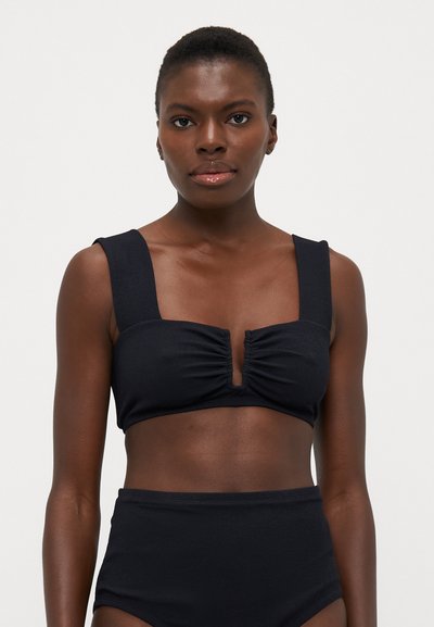 Zwart geribbeld bikini-top met brede banden en een geplooide voorkant, voorzien van een sleufuitsnijding. Met hoge taille zwarte onderkant maakt het de set compleet.