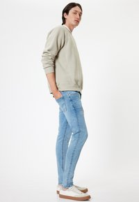 Felpa grigia chiara, jeans slim-fit azzurri chiari, sneakers bianche con accenti beige. Tessuto morbido, polsini a coste e cuciture piatte.
