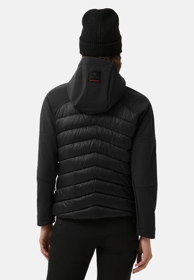 Černá bunda s kapucí, s prošívaným designem v tvaru chevronu a hladkým, matným materiálem. Nositá s černou pletenou čepicí.