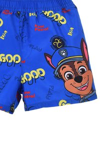 Shorts de bain bleus avec un personnage de chien en cartoon et des éléments de texte en rouge et jaune. Le matériau semble léger et respirant.