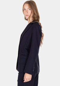 Blazer a righe sottili blu navy con una vestibilità sartoriale, revers a incavo e due tasche frontali. Presenta tre bottoni decorativi sulle maniche.