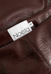 Burgundijska umetna usnjena tkanina s teksturo kamenčkov, z belim oznako z imenom "Noella" in velikostjo "S", prišito vanjo.