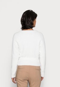 Witte trui met een zachte textuur, geribbelde structuur en een getailleerde taille. Lange mouwen en een brede halslijn maken het ontwerp compleet.