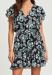 Vestido floral en negro, con flores en tonos verde azulado y blanco, escote en V, mangas con volantes y un dobladillo en capas con cintura ceñida.