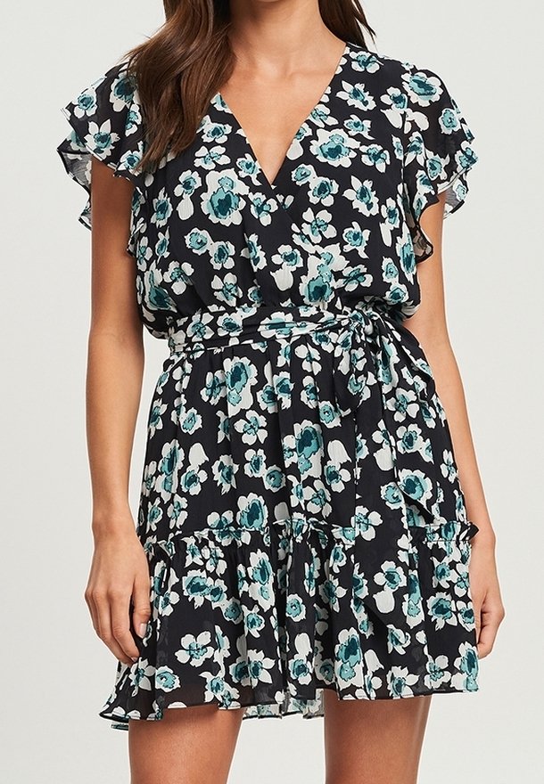 Vestido floral en negro, con flores en tonos verde azulado y blanco, escote en V, mangas con volantes y un dobladillo en capas con cintura ceñida.