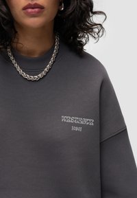 Kapuzenpullover in Anthrazitgrau aus Baumwollmischung, mit einem gerippten Rundhalsausschnitt und einem bedruckten Logo in kontrastierendem Hellgrau auf der Brust.