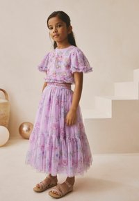 Vestido de dos piezas color lavanda con bordado floral, mangas con volantes y falda de tul en capas. Sandalias marrón claro completan el conjunto.