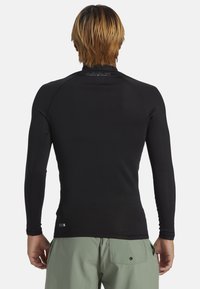 Rash guard negro de manga larga con un diseño ajustado, textura suave y mangas raglán. Presenta el logotipo de la marca en el cuello y el dobladillo inferior.