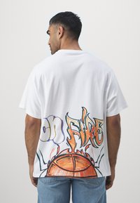 Biela bavlnená tričko s farebným graffiti textom "on FIRE" a grafikou basketbalovej lopty na chrbte. Krátke rukávy.