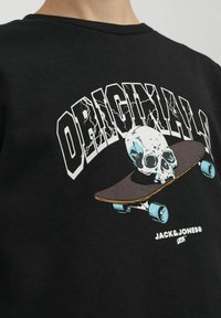 Felpa nera con grafica di un teschio su uno skateboard, con testo bianco audace che recita "ORIGINAL." Tessuto strutturato e design con collo a giro.