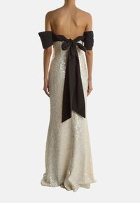 Ein schulterfreies Kleid aus cremefarbenem Stoff mit Paillettenverzierung, das auf der Rückseite mit einem großen schwarzen Satinband gebunden ist und eine elegante Silhouette schafft.