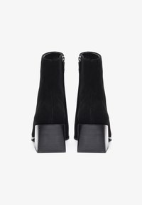 Botas de tobillo de gamuza negra con un alto tacón cuadrado. Cuentan con una cremallera suave en la parte trasera y una punta redondeada para una silueta moderna.