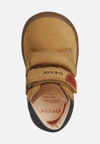Scarpa in pelle color tan per bambini, con due cinturini in Velcro, suola marrone e rivestimento del collare nero, vista dall'alto.