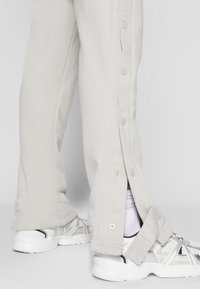 Light grey sweatpants with side snap buttons and a relaxed fit, paired with white athletic shoes and white socks visible at the cuff.
