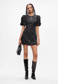 Crna mini haljina s napučenim rukavima, cvjetnim uzorkom, detaljem na dekolteu u obliku ključa. Nošena s crnim čizmama do koljena i clutch torbicom sa zakovicama.