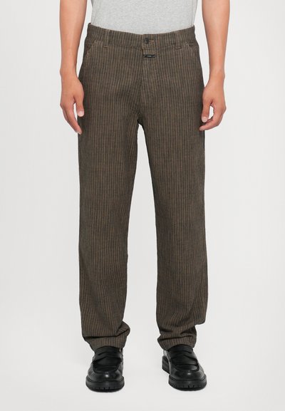 Pantaloni a righe verticali marroni con vestibilità rilassata, realizzati in tessuto testurizzato. Presentano una chiusura con bottone e tasche frontali. Indossati con scarpe nere.