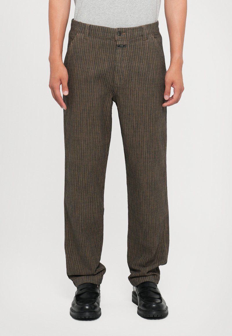 Brown vertical striped pants with a relaxed fit, made of textured fabric. Features a button closure and front pockets. Worn with black shoes.