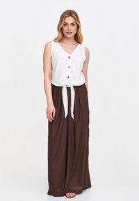 Biała bezrękawnikowa bluzka z drewnianymi guzikami zestawiona z brązową maxi spódnicą z wiązanym paskiem w talii. Gładki materiał, luźny krój, minimalistyczny styl.