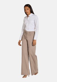 Witte button-up blouse met lange mouwen, gecombineerd met beige wijde broek en haksandalen, die een aansluitende silhouet en een soepele textuur toont.
