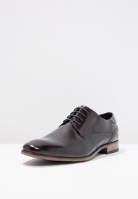 Chaussure habillée en cuir noir avec une finition lisse, bout rond, lacets et talon contrastant. Présente des coutures discrètes et un design moderne.
