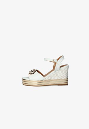 Sandali wedge bianchi con un accento circolare dorato e un lato in tessuto a fantasia. La suola presenta multiple strisce orizzontali in beige e oro.