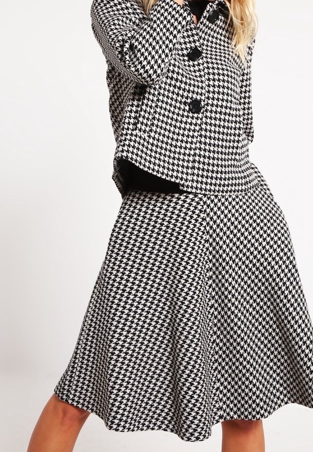 Ensemble ve vzoru černobílé houndstooth skládající se z dobře padnoucí bundy s velkými knoflíky a rozšířenou sukní, vyrobené z texturované látky.