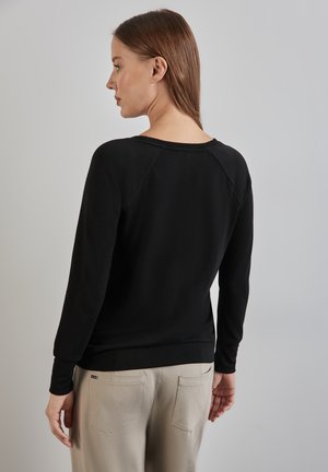 Maglione nero a maniche lunghe con vestibilità rilassata, caratterizzato da maniche raglan e scollatura rotonda, abbinato a pantaloni beige.