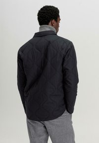 Gestepptes schwarzes Hemdjackett mit Wellenmuster, mit einem grauen hohen Kragen und einer lockeren Passform, von hinten betrachtet.