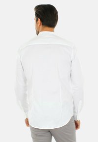 Camicetta bianca a maniche lunghe con colletto button-down e orlo curvo. Realizzata in un materiale liscio, presenta un design pulito e minimalista.