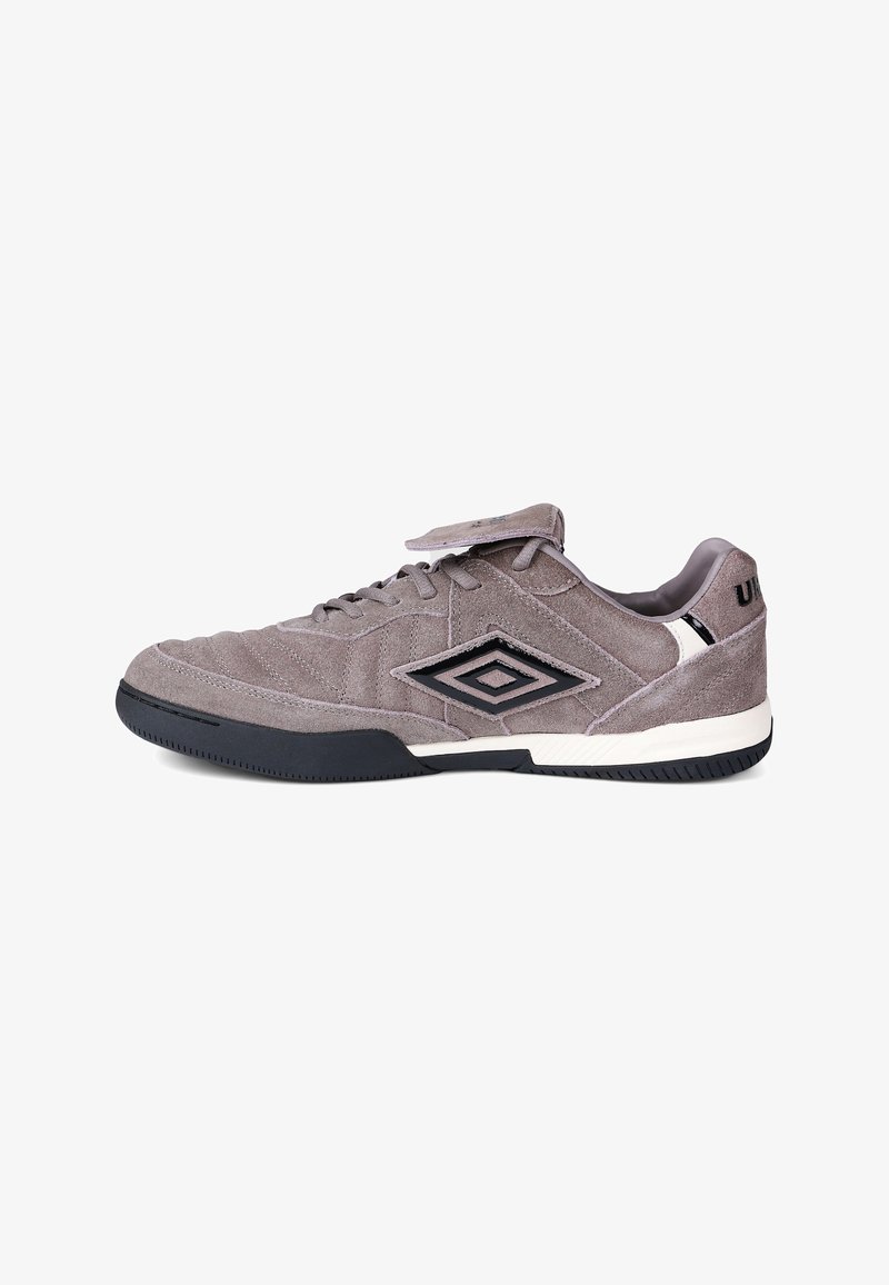 Chaussure de sport en daim gris avec semelle noire et blanche, logo double losange noir sur le côté, lacets, et languette repliée.