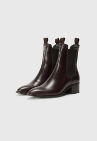 Bottines Chelsea en cuir marron avec une finition lisse, des bouts pointus, des panneaux latéraux élastiques et des languettes pour un enfilage facile. Design à talon bloc.