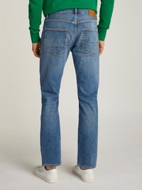 Light blue denim jeans with a straight fit, back pockets, and a leather patch at the waistband. Paired with white sneakers on a neutral background.