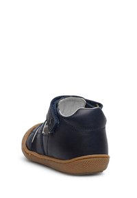 Dětská bota v námořnické modré barvě z kůže s texturovaným povrchem, nastavitelným páskem a gumovou podrážkou. Obsahuje bílé švy a kulatou špičku.