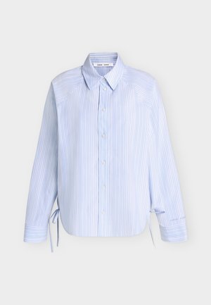 Ανοιχτό μπλε μακρυμάνικο πουκάμισο με κάθετες λευκές ρίγες, κλείσιμο με κουμπιά μπροστά, μυτερό γιακά και κορδόνια και στις δύο πλευρές κοντά στο τελείωμα.