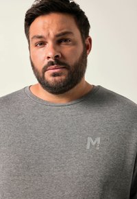 T-shirt grigio a maniche corte con scollo rotondo e un sottile logo "M" sul petto. Tessuto morbido, vestibilità casual.