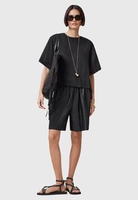 Svart linneöverdel med vida ärmar, i kombination med svarta lädershorts. Tillbehören inkluderar en texturerad svart väska och strap-on svarta sandaler.