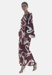 Outfit a fantasia bordeaux e bianca con maniche ampie e pantaloni larghi, realizzato in tessuto morbido, accompagnato da sandali con cinturino.