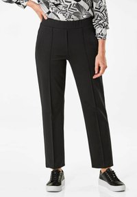 Zwarte broek met een gladde textuur, voorzien van voorplooien, een hoge tailleband en zijzakken, gecombineerd met zwarte sneakers.