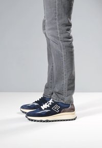 Marineblaue Sneaker aus Wildleder und Netzmaterialien, weiße Schnürsenkel, eine graue Rückseite und schwarze Details an der Gummisohle.