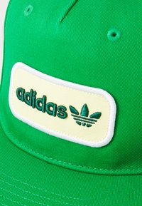 Green baseball cap with a yellow embroidered logo patch, featuring the text "adidas" and a three-leaf emblem, crafted from textured fabric.
