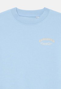 Světle modrý crewneck svetr s rebrovaným límcem a malým béžovým logem "Jack & Jones Denim Crew Collective" na levé straně hrudi.