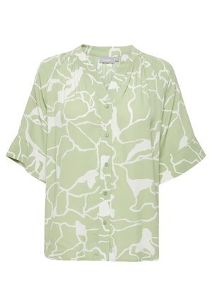 Blouse verte à manches courtes avec un motif abstrait blanc, fermeture à boutons sur le devant et coupe décontractée. Fabriquée en tissu léger avec une texture lisse.