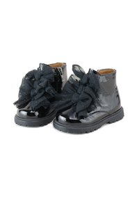 Botines de charol negro con grandes lazos de tul negro en la parte frontal, suela de goma y cremallera lateral para facilitar su uso.