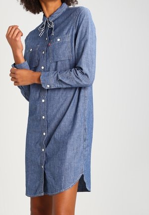 Robe chemise en denim avec boutonnage sur le devant, manches longues, deux poches poitrine et ourlet arrondi ; dotée d'un col pointu et d'un ruban décoratif.