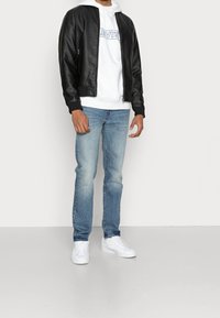 Chaqueta bomber de cuero negro con puños acanalados, sudadera blanca con logo impreso, jeans azul claro y zapatillas blancas. Atuendo casual.