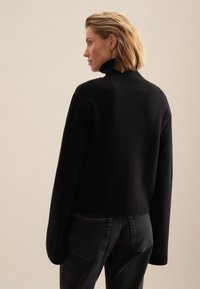 Czarny sweter z golfem o luźnym, oversize'owym kroju, wykonany z miękkiego materiału. Noszony z ciemnymi dżinsami, widok z tyłu.