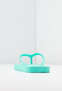 Turquoise flip-flop with a heart-shaped strap design, made of flexible rubbery material. Features a flat sole with textured edges.
