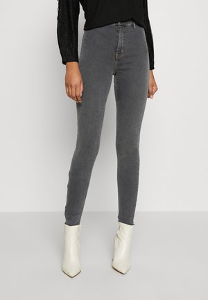 Kvinde iført grå skinny jeans med høj talje, kombineret med hvide ankelstøvler med spids tå og en sort langærmet top.