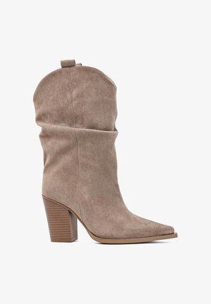 Botte beige en daim mi-mollet avec un bout pointu, une tige souple et un talon bloc empilé sur fond blanc.
