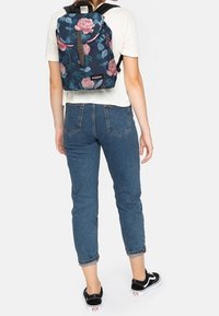 Tmavě modrý batoh s květinovým vzorem, kulatým vrškem, hnědou přezkou a nastavitelnými černými popruhy. Nositelný s modrými džínami s vysokým pasem a černými teniskami.